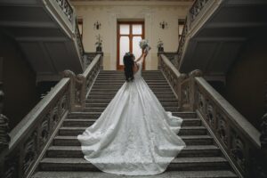 Bride wearing an elegant lace wedding gown with a dramatic train on a grand staircase, showcasing bridal gown inspiration for brides searching for beautiful wedding dresses.