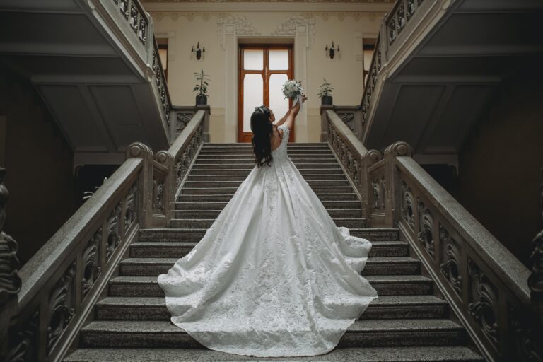 Bride wearing an elegant lace wedding gown with a dramatic train on a grand staircase, showcasing bridal gown inspiration for brides searching for beautiful wedding dresses.