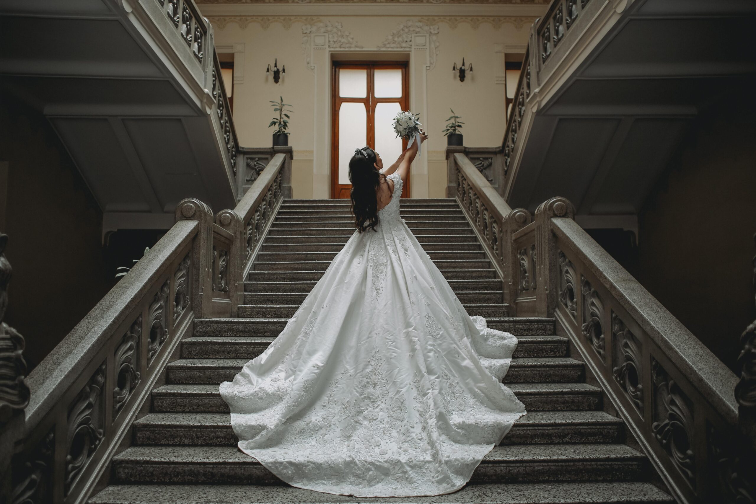 Bride wearing an elegant lace wedding gown with a dramatic train on a grand staircase, showcasing bridal gown inspiration for brides searching for beautiful wedding dresses.