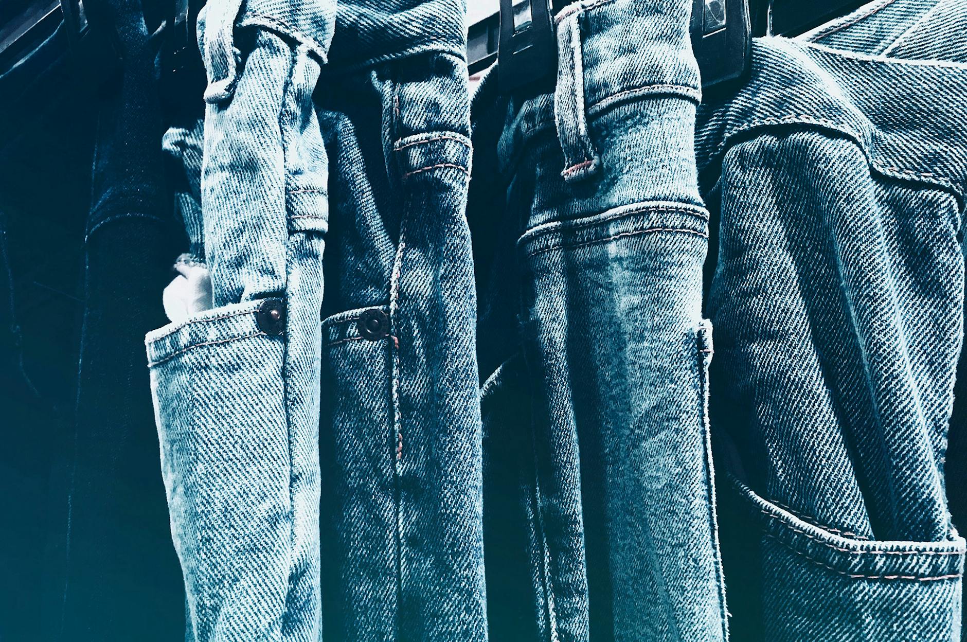 Close-up of denim jeans hanging on a rack, showing different washes and textures.