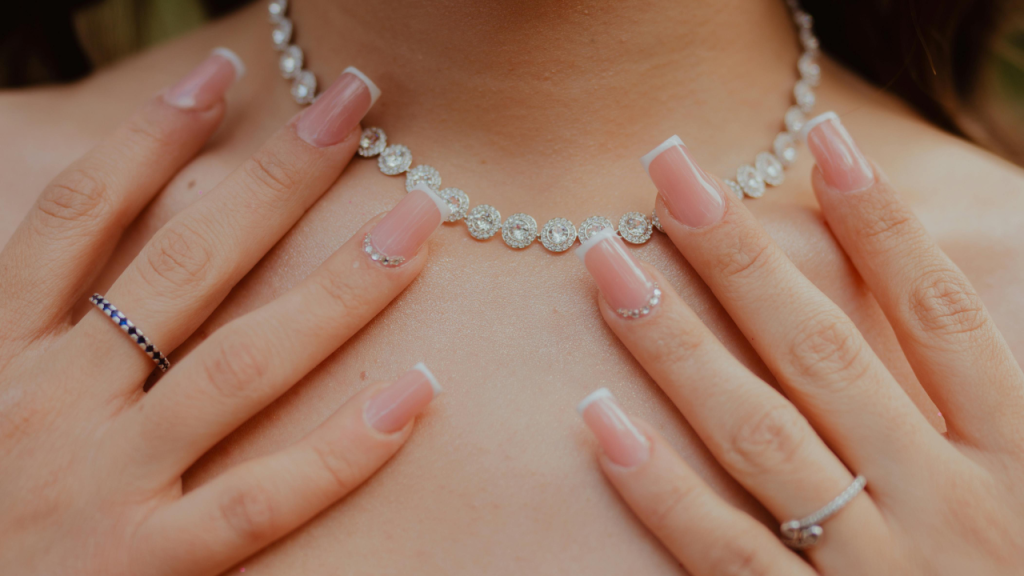 Close-up of a bride wearing a sparkling diamond necklace with manicured hands and rings, showcasing elegant bridal accessories.