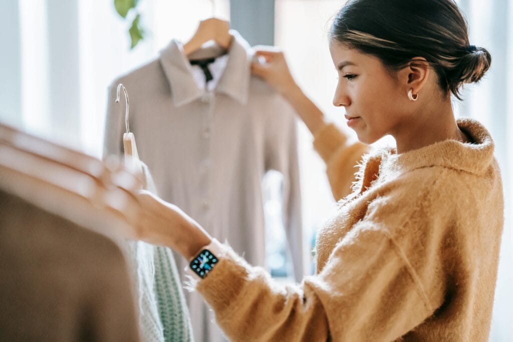 Petite woman choosing outfits from a clothing rack at home, illustrating styling tips and outfit ideas for petite women.