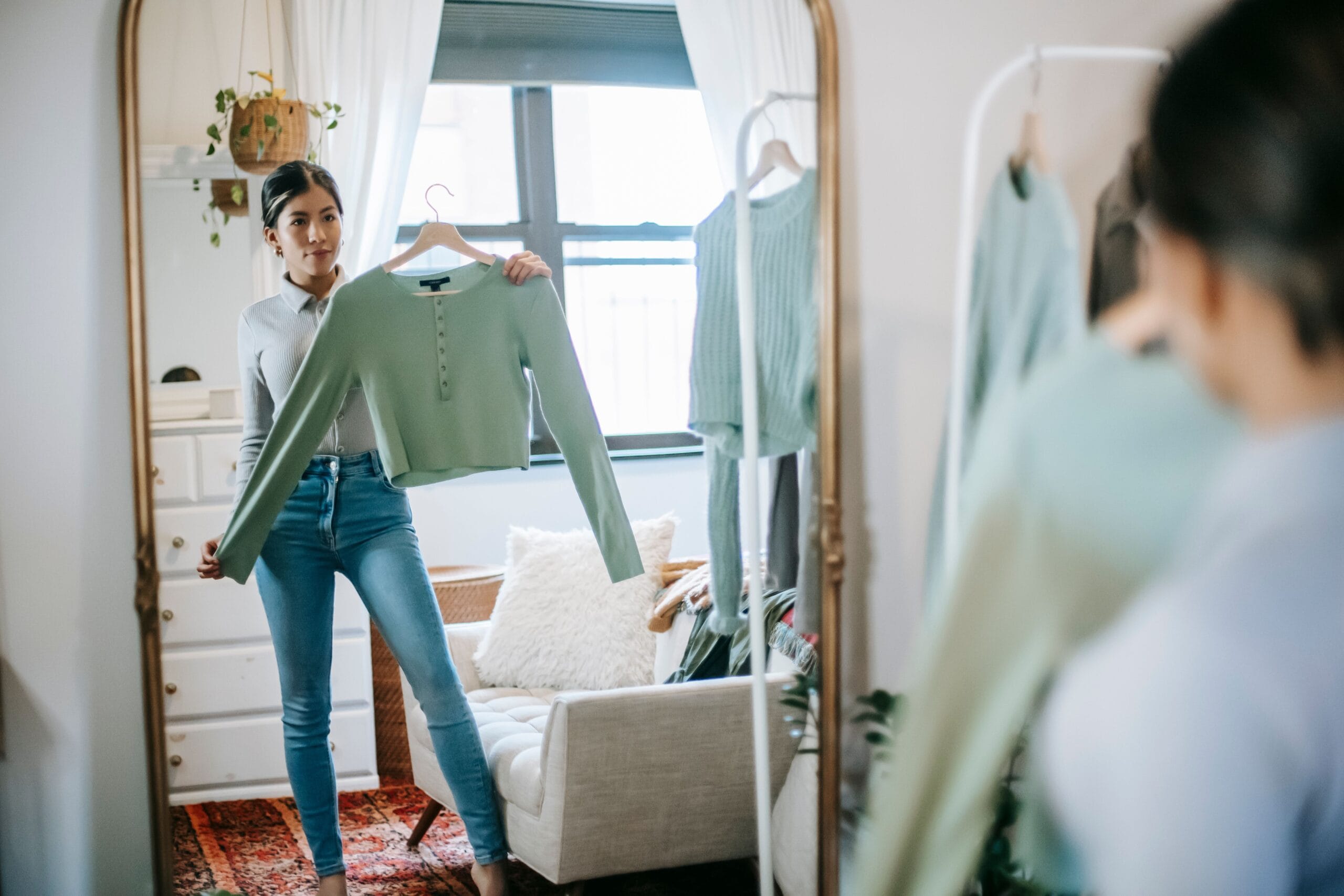 Woman choosing an outfit in front of a mirror while exploring how to find your personal style and create new outfits from existing wardrobe.