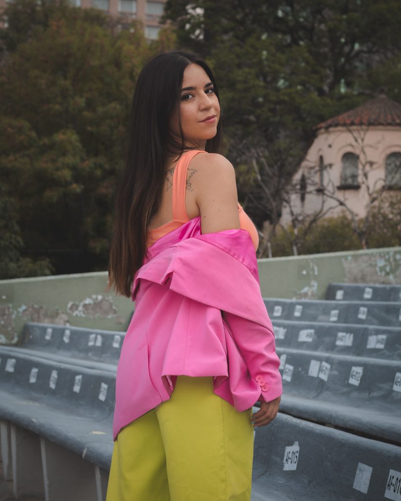 Woman wearing a bright pink oversized shirt over a coral top with lime-green trousers, illustrating color mistakes that can make outfits look messy and less expensive due to clashing colors.