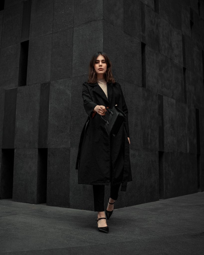 A woman wearing a polished monochrome outfit with a long black coat, black pants, and pointed-toe shoes for a sophisticated, put-together look.