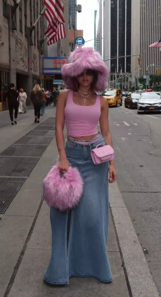 Woman wearing a pink crop top, long denim skirt, oversized pink furry hat, matching furry handbag, and pink crossbody bag, illustrating how overstyling can make outfits look less expensive.