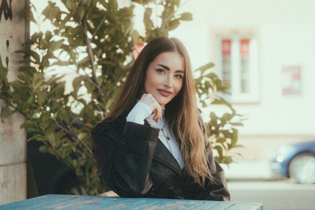 woman in black blazer sitting outdoors with soft sunlight, demonstrating elegant styling and psychological fashion tricks to look more attractive and confident