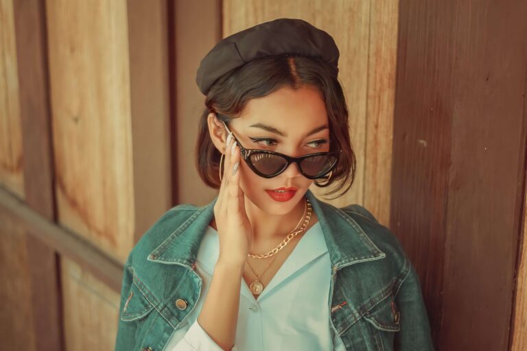 Petite woman wearing stylish sunglasses, layered necklaces, hoop earrings, and a beret demonstrating flattering accessories for petite women.