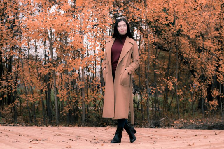 Woman wearing a camel coat, burgundy sweater, black jeans, and ankle boots styled as a chic fall outfit for a perfect fall wardrobe.