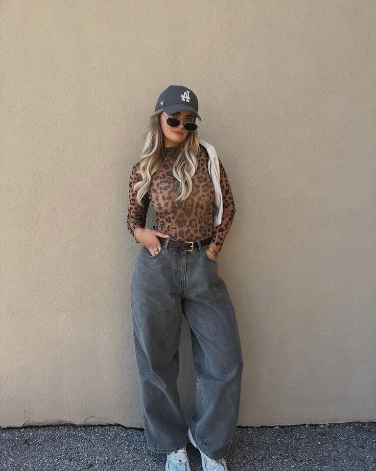 Woman wearing a gray animal print top with gray wide-leg jeans, a gray cap, and white sneakers, showing how to style gray with animal print outfits.