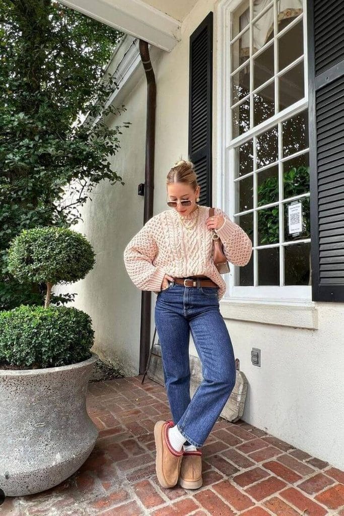 Woman wearing a chunky cable-knit sweater with straight-leg jeans, a brown belt, and tan ankle boots for a sweater and jeans outfit.