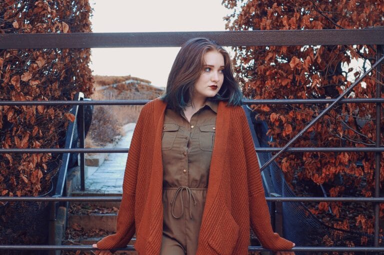Woman wearing a rust-colored cardigan and brown fall outfit outdoors surrounded by autumn trees, showcasing fall outfit ideas.