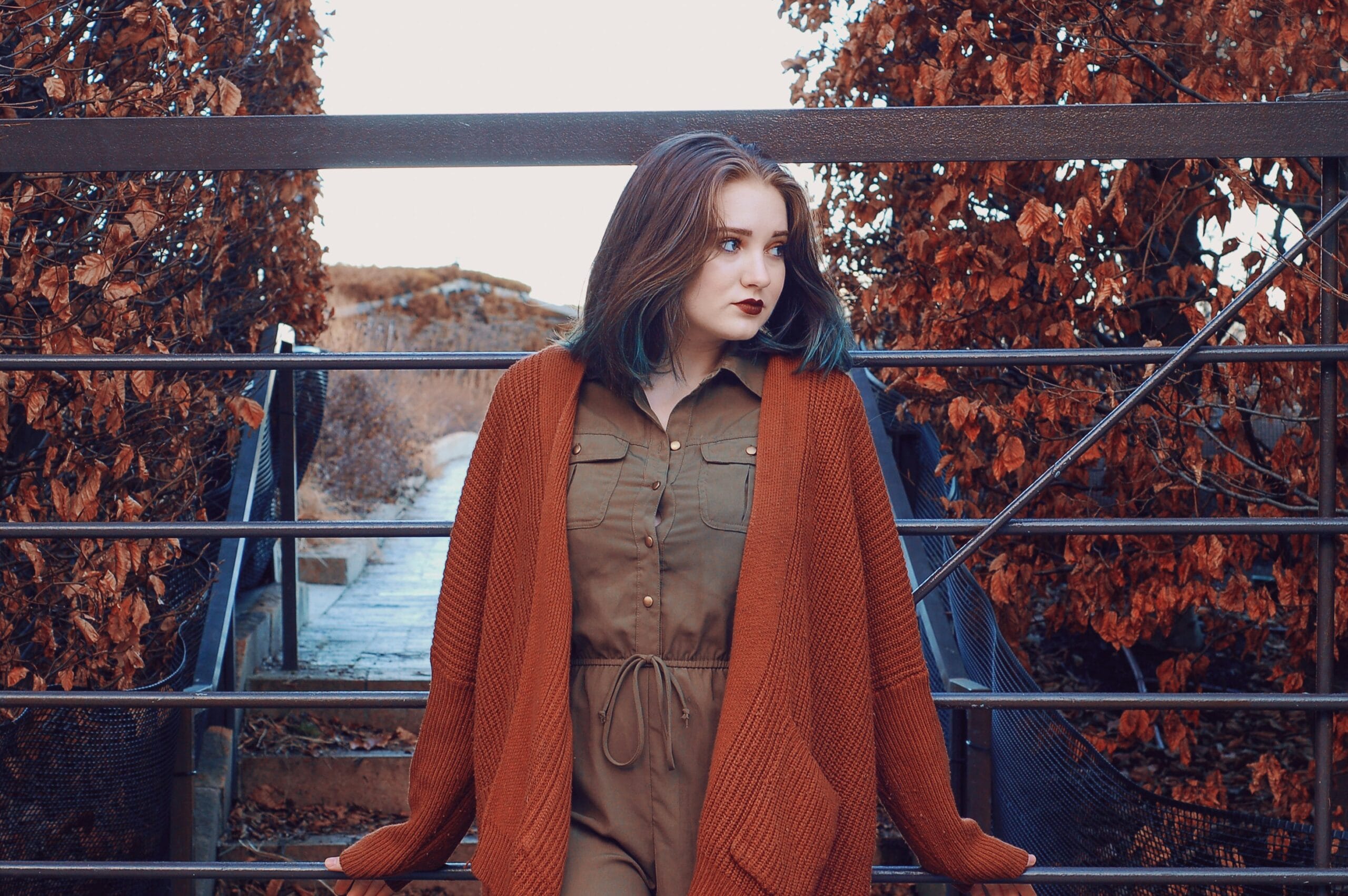 Woman wearing a rust-colored cardigan and brown fall outfit outdoors surrounded by autumn trees, showcasing fall outfit ideas.