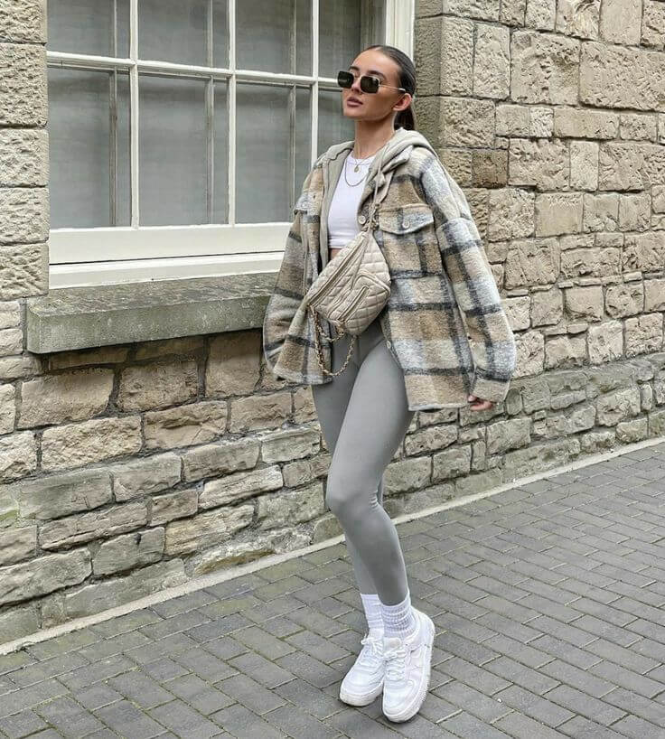 Woman wearing a plaid shacket over a white top with gray leggings and white sneakers for a casual shacket outfit idea.