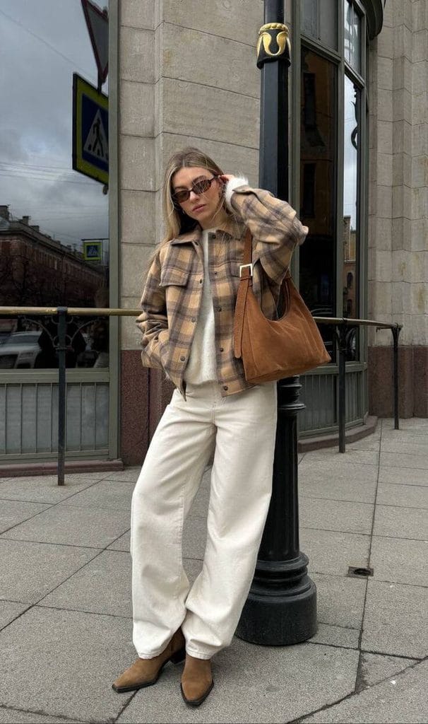 Woman wearing a plaid shacket over a light sweater with white jeans and brown ankle boots for a casual shacket outfit idea
