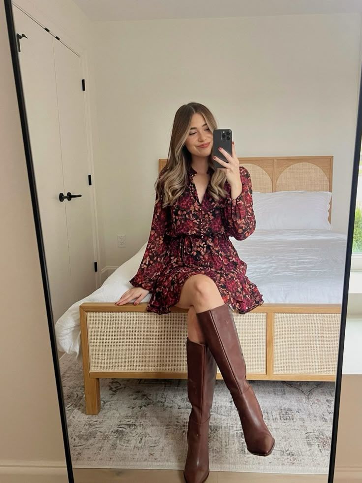 Woman wearing a burgundy floral mini dress with long sleeves and brown knee-high boots, posing in front of a mirror for a dress and boots outfit for Thanksgiving dinner.