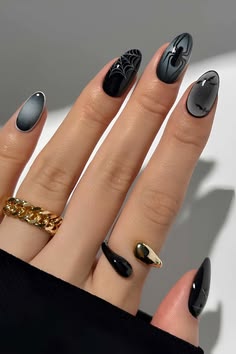 A hand featuring black and gray Halloween nail art with spiderweb designs on accent nails, tiny black spiders, and glossy dark polish on short almond-shaped nails, showcasing spiderweb Halloween nail art and fall nail ideas.