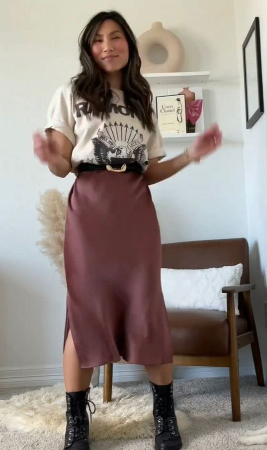 Woman wearing a graphic T-shirt tucked into a burgundy satin midi skirt with black combat boots, showing how to style a Halloween T-shirt with a satin skirt for a seasonal outfit.