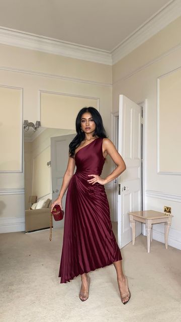 Woman wearing a burgundy satin one-shoulder midi dress with matching heels and a red handbag, showcasing a jewel-tone dress outfit for Thanksgiving dinner.