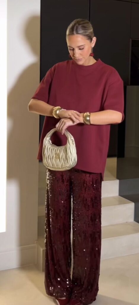 Woman wearing a burgundy short-sleeve top with matching burgundy sequin pants and a gold handbag, showcasing a matching two-piece outfit for Thanksgiving dinner.