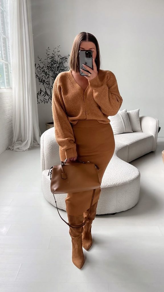 Woman wearing a camel-colored cardigan, matching brown skirt, and brown knee-high boots, showcasing a monochrome outfit for Thanksgiving dinner.