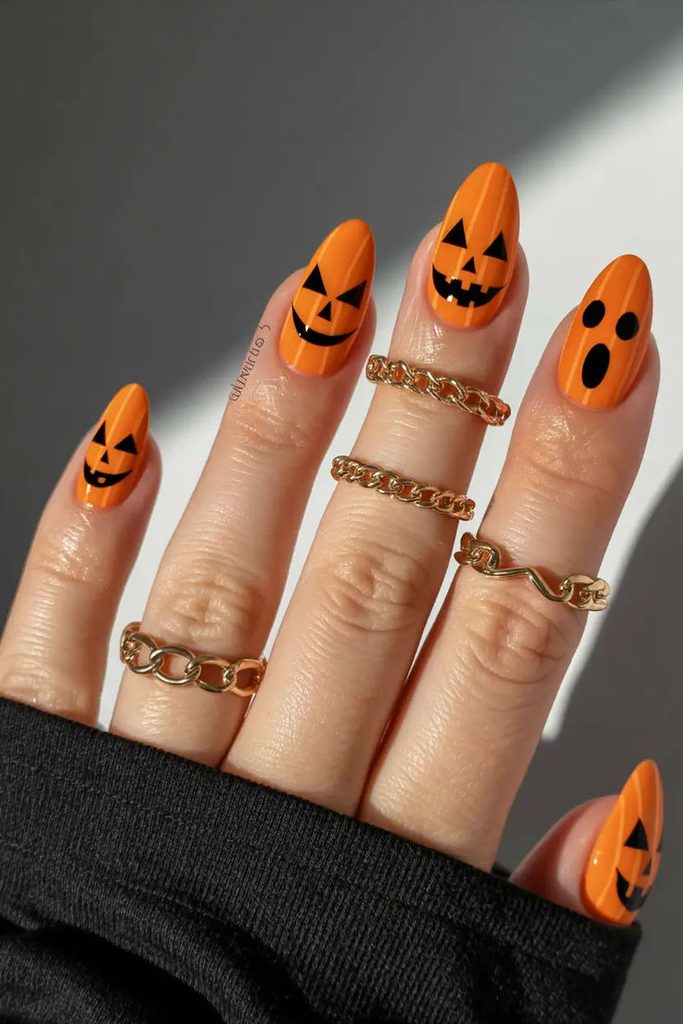 Bright orange pumpkin Halloween nail art featuring black jack-o’-lantern faces and spooky expressions on long, almond-shaped nails, a fun Halloween nail idea for fall.