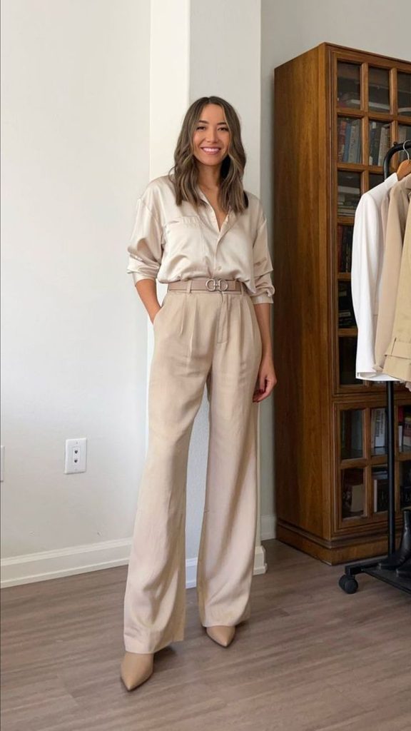 Woman wearing a cream satin blouse tucked into matching beige tailored pants with a belt and pointed-toe heels, showcasing an elegant silk blouse and tailored pants outfit for Thanksgiving dinner.