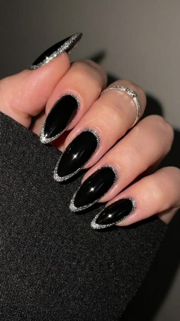 Glossy black almond-shaped nails with silver glitter borders around each nail, showcasing silver glitter border black nails for Halloween and an elegant fall nail idea.