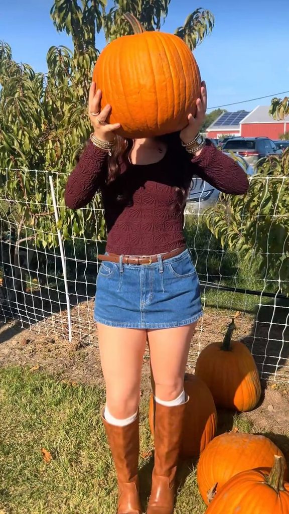 Sweater and skirt outfit for pumpkin patch featuring a burgundy sweater, denim mini skirt, and brown knee-high boots.
