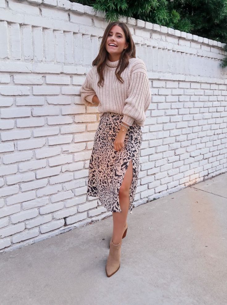 Woman wearing a cream knit sweater, a leopard-print midi skirt with a side slit, and beige ankle boots for a stylish Thanksgiving dinner outfit.