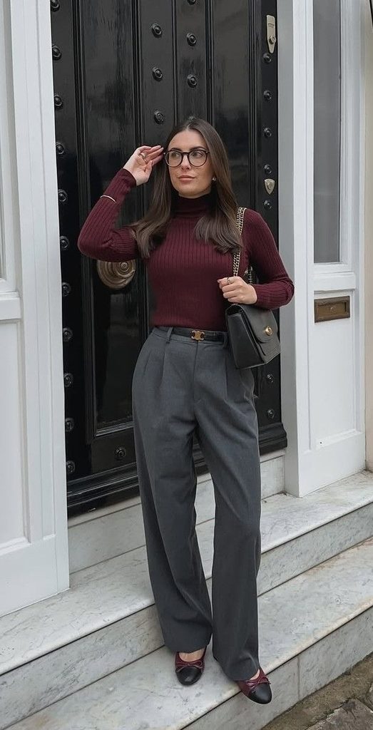 Woman wearing a burgundy turtleneck and gray tailored pants with burgundy-accented flats and a black handbag, showcasing a turtleneck and tailored pants outfit for Thanksgiving dinner.